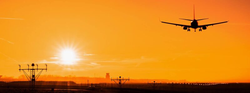 Sylwetka samolotu lądującego o zachodzie słońca na lotnisku Kraków Balice
